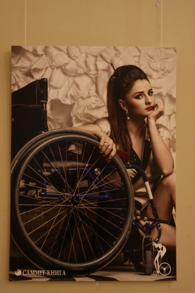 “Можемо бути привабливими і успішними” – показують виставку з красунями на інвалідному візку (ФОТО). дівчина, красуня, фотовиставка нескорена краса, інвалідний візок, інвалідність, wall, wheel, bicycle, indoor, person, land vehicle, clothing, bicycle wheel, tire, woman. A woman standing in front of a bicycle
